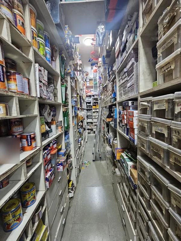 Stock aisle at Mahalaxmi Hardware and Electricals with paint tins, pigment colours and boxed hardware fittings