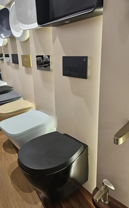 Wall-hung WCs in black, white, beige and grey, with flush plates above, at Mahalaxmi Ceramics
